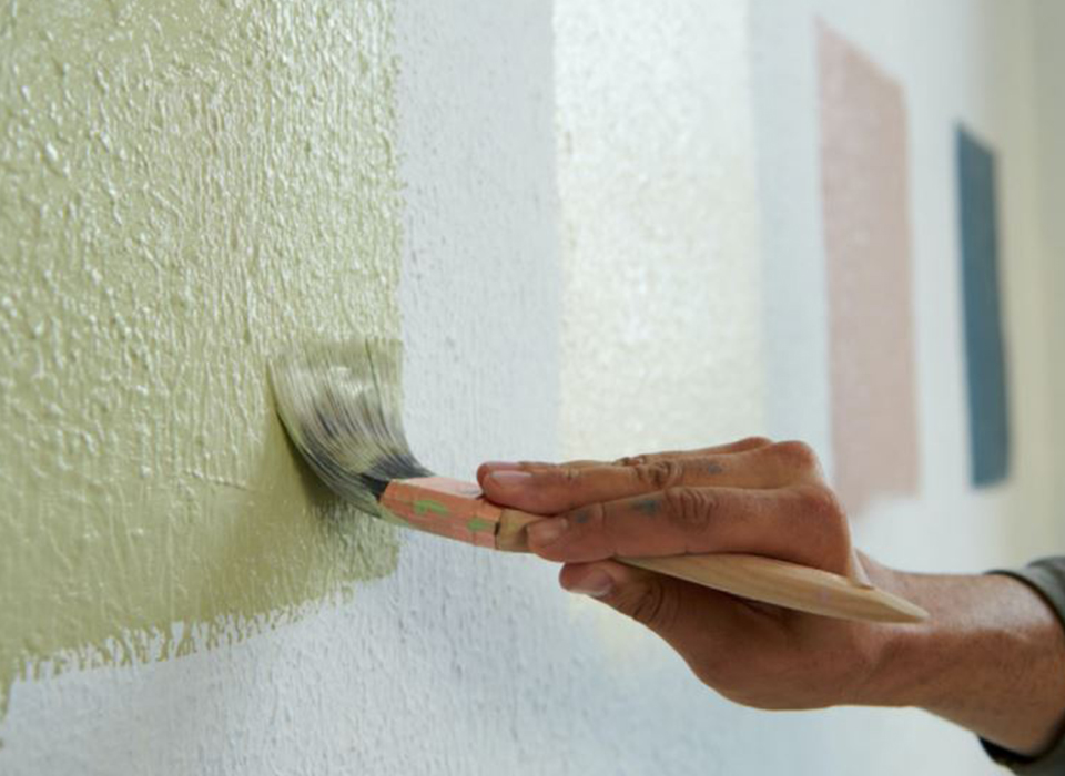 Painting wall green with brush. Color swatches on wall in background.