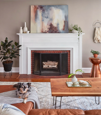 Living room with central, white, wood-burning fireplace, Winter Calm walls and abstract art on mantel.  